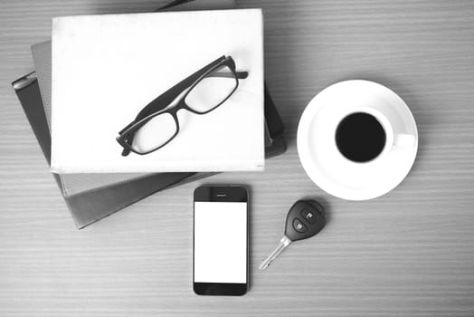 coffee,phone,car key,eyeglasses and stack of book on wood table background  black  and white color