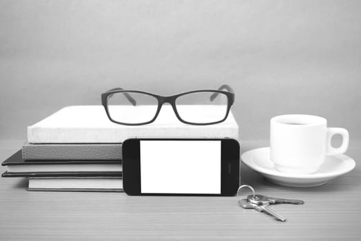 coffee,phone,key,eyeglasses and stack of book on wood table background black  and white color