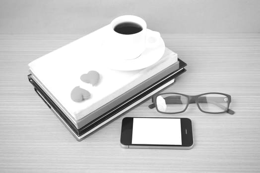 coffee,phone,eyeglasses,stack of book and heart on wood table background black  and white color