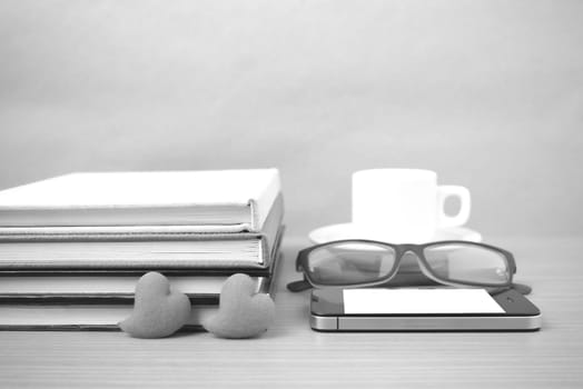 coffee,phone,eyeglasses,stack of book and heart on wood table background black  and white color