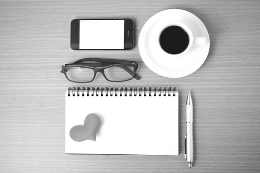 coffee,phone,eyeglasses,notepad and heart on wood table background black  and white color
