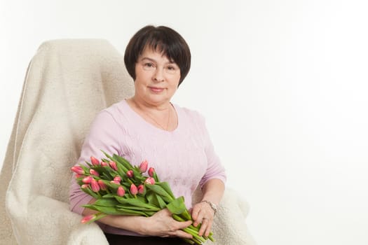 the beautiful mature woman sits on a chair with a bouquet of tulips