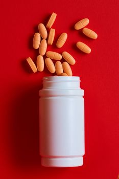 Pills spilling out of pill bottle on red. Top view with copy space. Medicine concept. Shallow dof