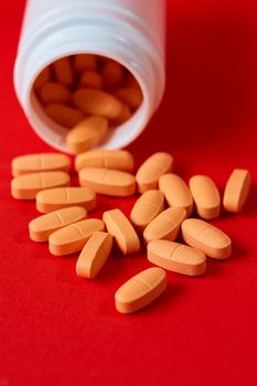 Pills spilling out of pill bottle on red. Top view with copy space. Medicine concept. Shallow dof