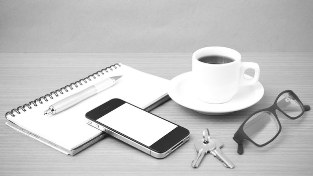 coffee,phone,notepad,eyeglasses and key on wood table background black and white color