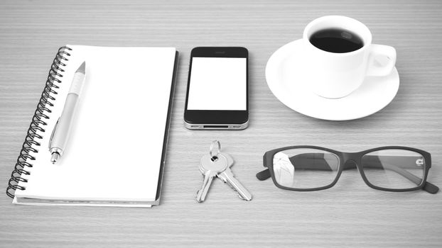 coffee,phone,notepad,eyeglasses and key on wood table background black and white color