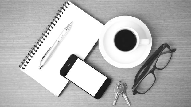 coffee,phone,notepad,eyeglasses and key on wood table background black and white color