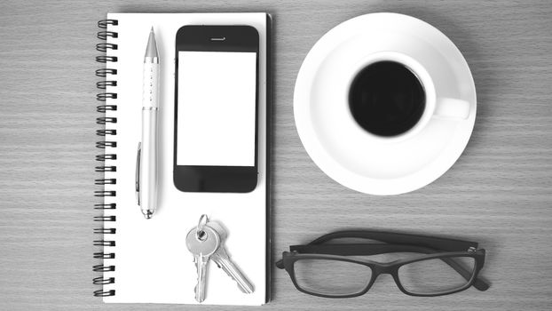 coffee,phone,notepad,eyeglasses and key on wood table background black and white color