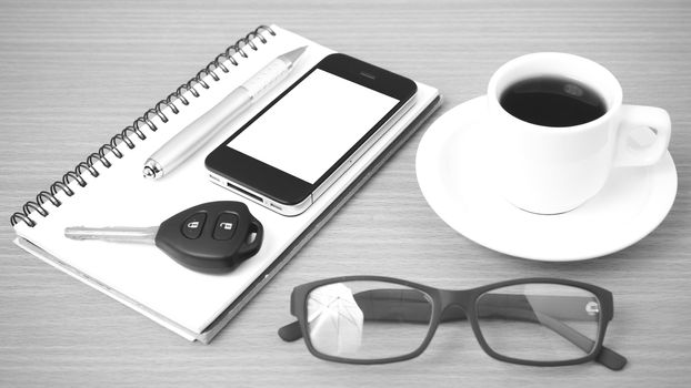 coffee,phone,notepad,eyeglasses and car key on wood table background black and white color