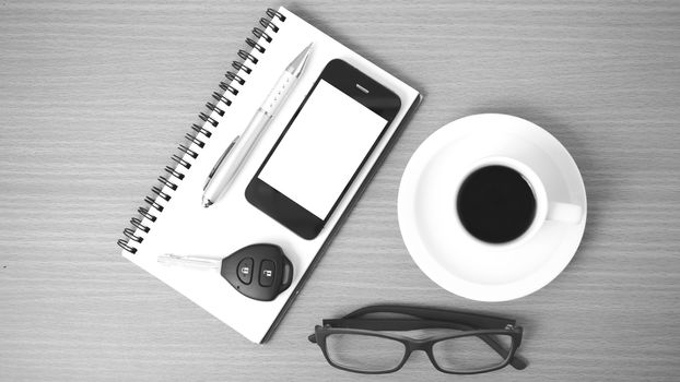 coffee,phone,notepad,eyeglasses and car key on wood table background black and white color