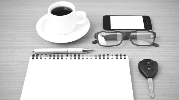 coffee,phone,notepad,eyeglasses and car key on wood table background black and white color