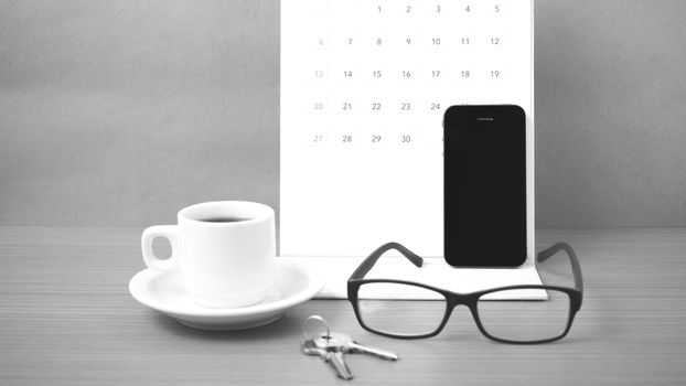 coffee,phone,eyeglasses,calendar and key on wood table background black and white color