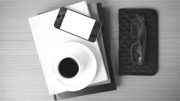 coffee,phone,eyeglasses,stack of book and wallet on wood table background black and white color