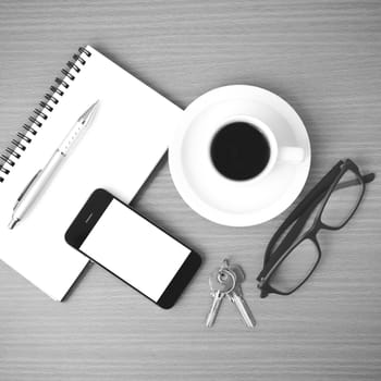 coffee,phone,notepad,eyeglasses and key on wood table background black and white color