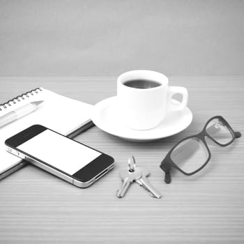 coffee,phone,notepad,eyeglasses and key on wood table background black and white color