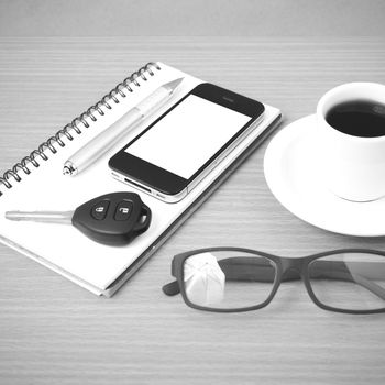 coffee,phone,notepad,eyeglasses and car key on wood table background black and white color