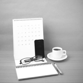 coffee,phone,eyeglasses,notepad and canlendar on wood table background black and white color