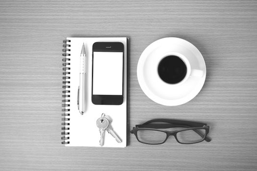 coffee,phone,notepad,eyeglasses and key on wood table background black and white color