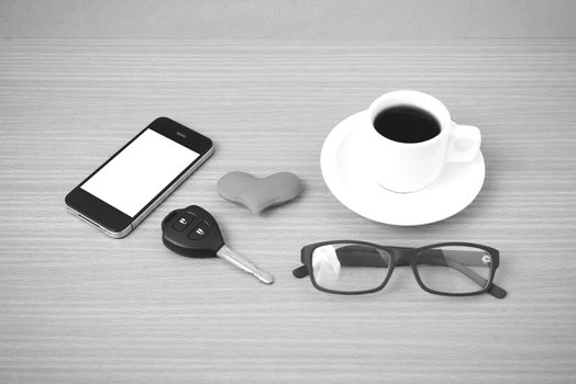 coffee,phone,eyeglasses and car key on wood table background black and white color