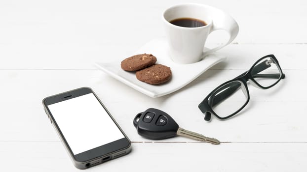 coffee cup with cookie,phone,eyeglasses and car key on white wood table
