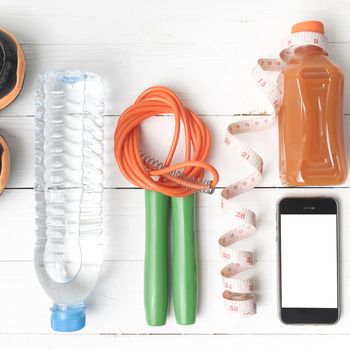 fitness equipment:running shoes,phone,measuring tape,water,juice and jumpong rope on white wood background