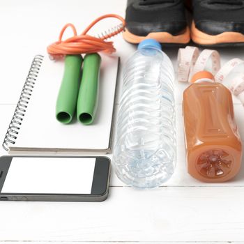 fitness equipment:running shoes,jumping rope,notepad,phone,water,juice and measuring tape on white wood background