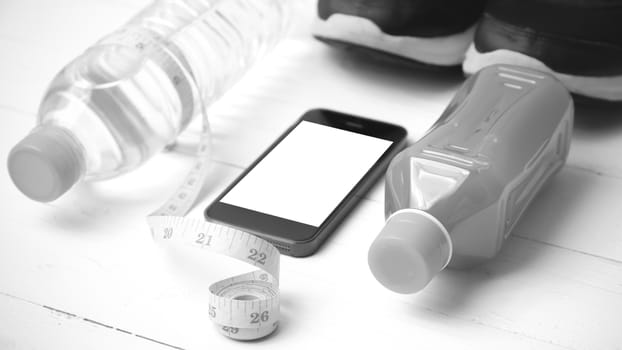 fitness equipment:running shoes,measuring tape,water,juice and phone on white wood background black and white color