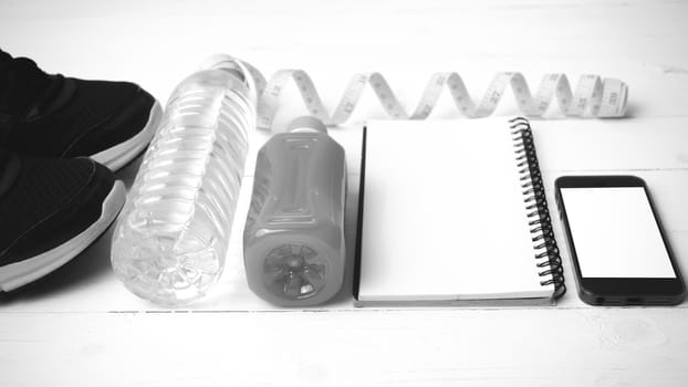 fitness equipment:running shoes,water,measuring tape,notepad,phone and juice on white wood background black and white color