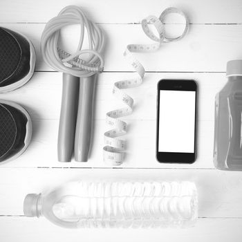 fitness equipment:running shoes,phone,measuring tape,water,juice and jumpong rope on white wood background black and white color