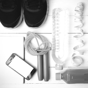 fitness equipment:running shoes,jumping rope,notepad,phone,water,juice and measuring tape on white wood background black and white color