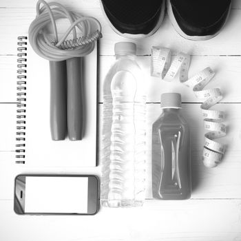 fitness equipment:running shoes,jumping rope,notepad,phone,water,juice and measuring tape on white wood background black and white color
