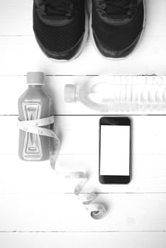 fitness equipment:running shoes,measuring tape,water,juice and phone on white wood background black and white color