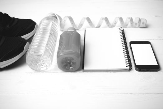 fitness equipment:running shoes,water,measuring tape,notepad,phone and juice on white wood background black and white color