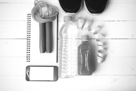 fitness equipment:running shoes,jumping rope,notepad,phone,water,juice and measuring tape on white wood background black and white color