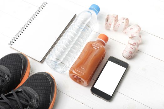 fitness equipment:running shoes,water,measuring tape,notepad,phone and juice on white wood background