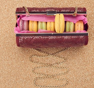 Macarons french in handbag. Luxury shiny glamor fashion clutch. Sweet colorful dessert. Unusual creative art, gold party background, bokeh, copyspase. Vintage