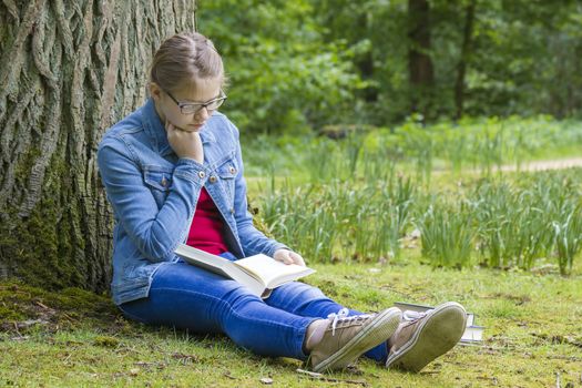 Young girl reading book in park in spring day