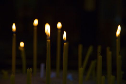 Lighted wax candles in a church burning in the twilight