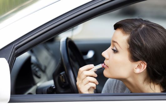 Pretty young woman in a car doing makeup while standing in a road jam