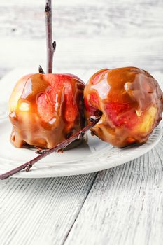 Ripe apples with toffee caramel decorated with branch on a light background.