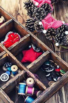 Wooden box with buttons and thread on a background of a wreath from pine cones