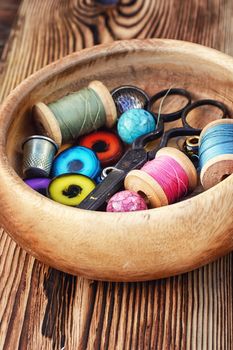 Scissors,buttons and thread in wooden bowl on background of pine.