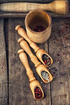 Three kinds of pepper in wooden spoons on vintage background