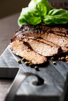 Close up sliced medium grilled beef steak with pepper and oregano leafs on marble meat cutting board on dark stone background