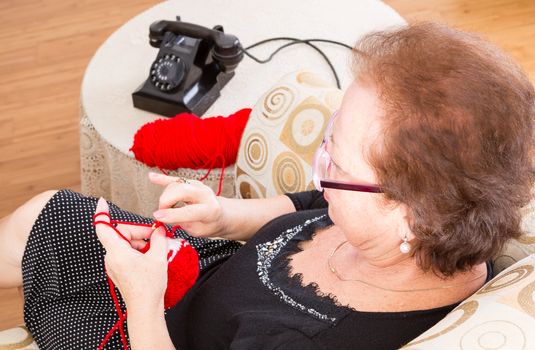 Grandma sitting knitting on a couch in the living room near the old-fashioned rotary telephone as she waits for a call, view from above