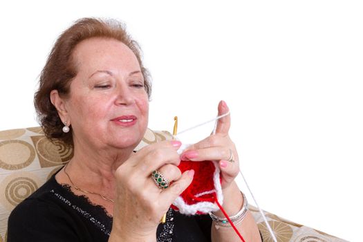 Attractive elderly woman sitting in an armchair concentrating on her knitting as she keeps herself young through her hobbies, isolated on white