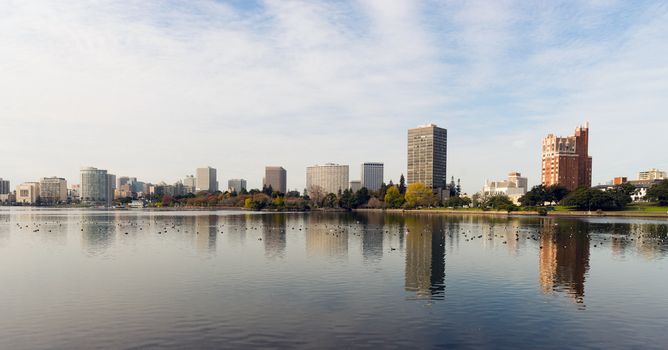An overcast sky is reflected in the smooth water of Lake Merritt in front of Oakland 