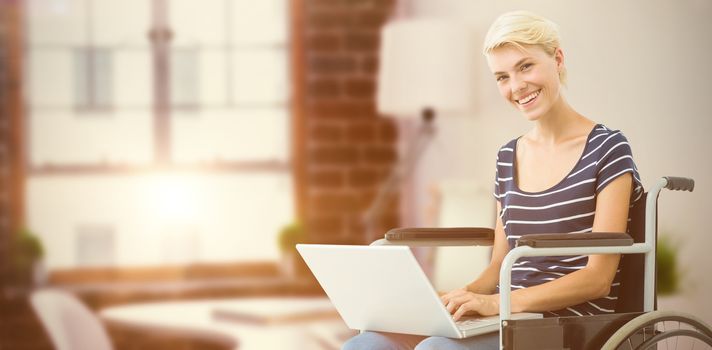 Woman in wheelchair using computer against laptop on desk with glasses and notepad