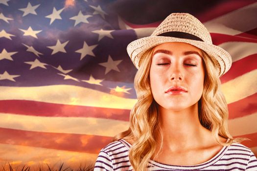 Gorgeous blonde hipster with straw hat against digitally generated american flag rippling over grass