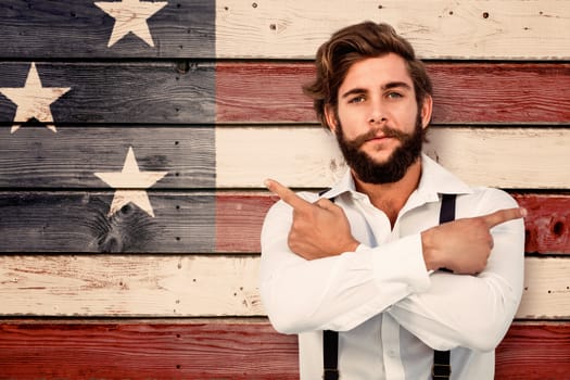 Confident hipster pointing sideways with arms crossed against composite image of usa national flag